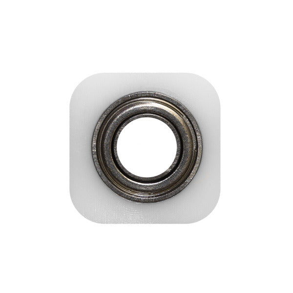 Metal bearing with white square backing block mounted on plain background.