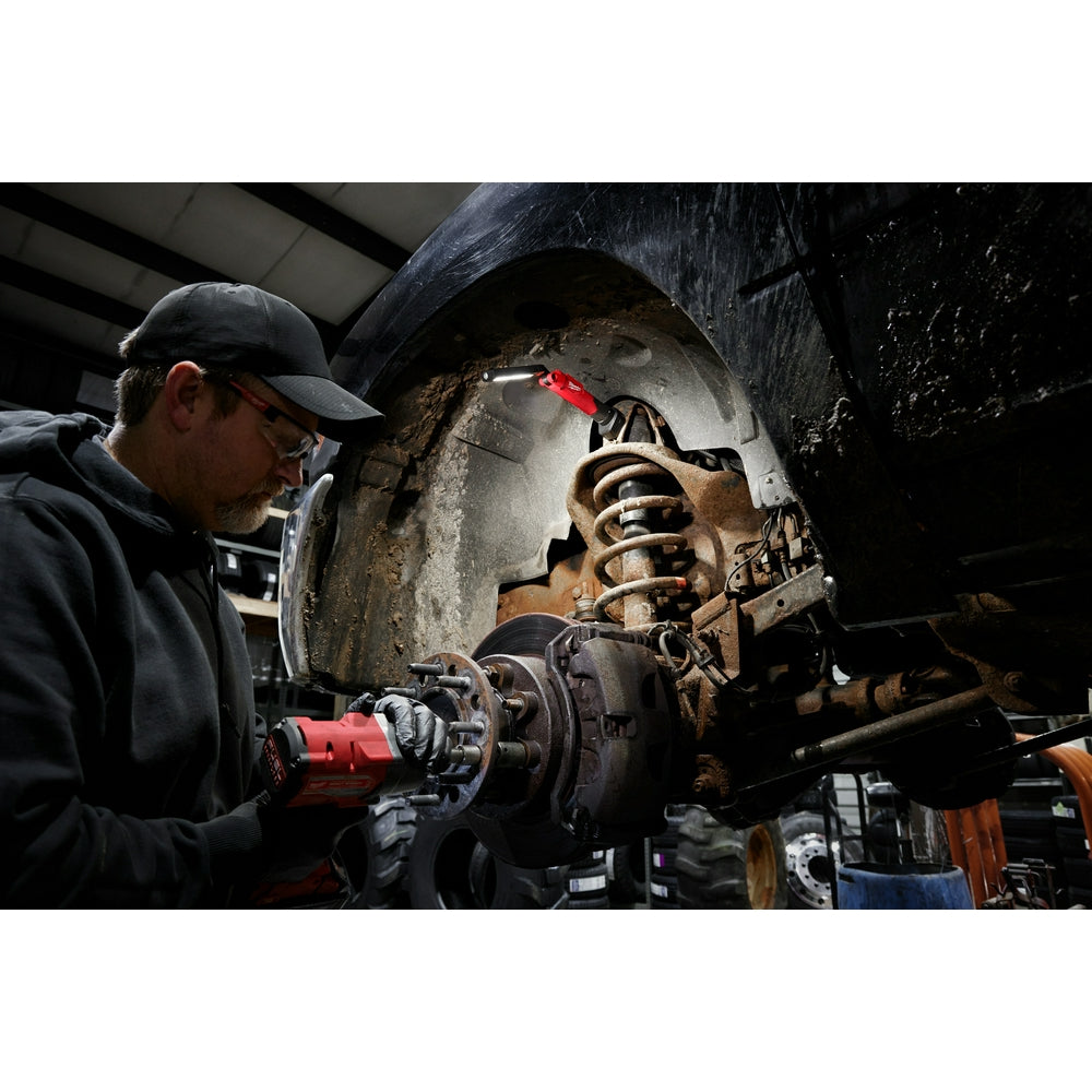 Red stick light with magnet attached to vehicle undercarriage during nighttime maintenance work.