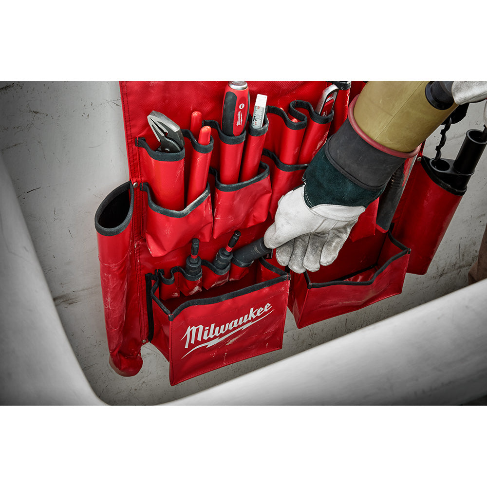 Red Milwaukee tool apron with multiple pockets and black straps holding various hand tools and accessories.