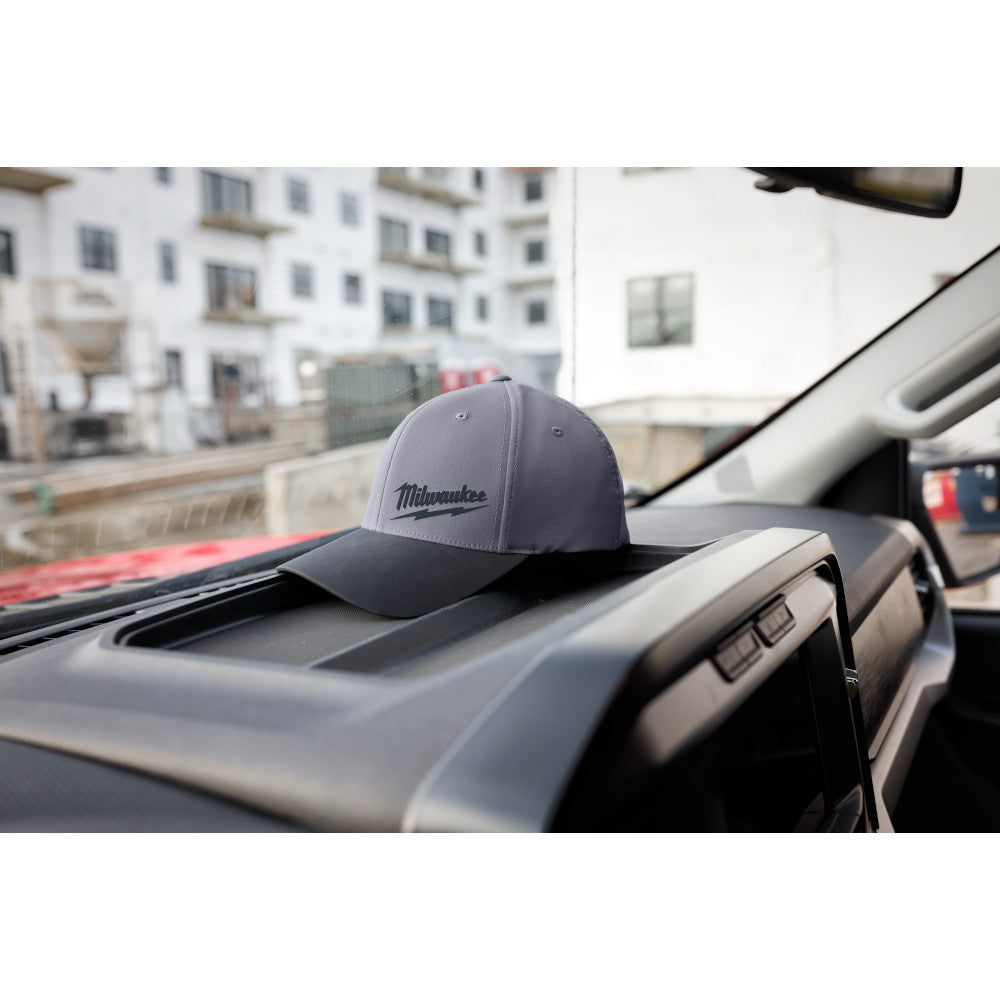 Dark gray fitted baseball cap with Milwaukee logo on crown, displayed on vehicle dashboard.