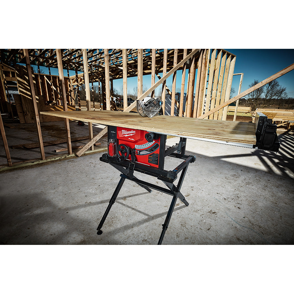 Red and black Milwaukee folding table saw stand with extending support rails on construction site.