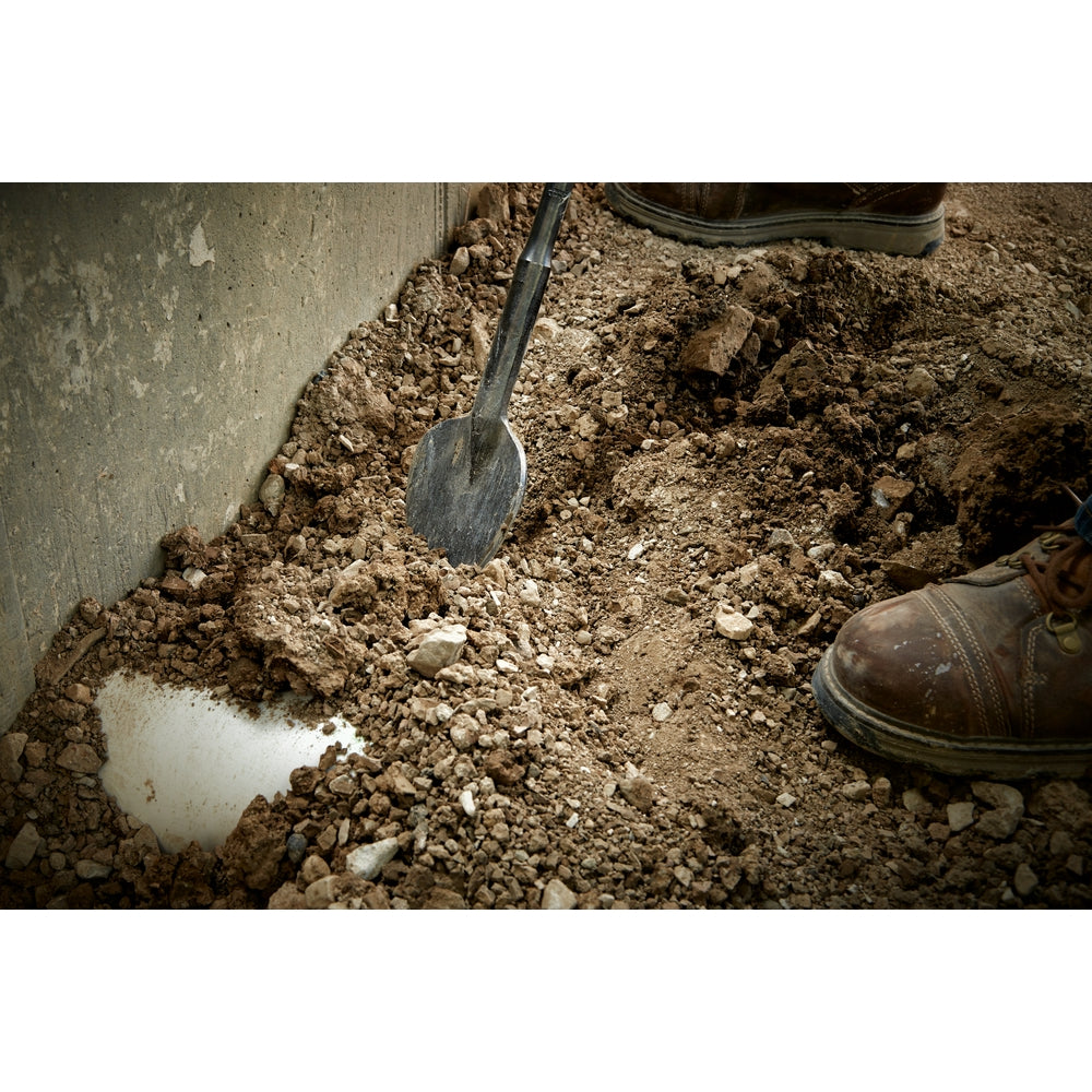 SDS-Max clay spade with rectangular blade in soil and gravel, work boot visible.
