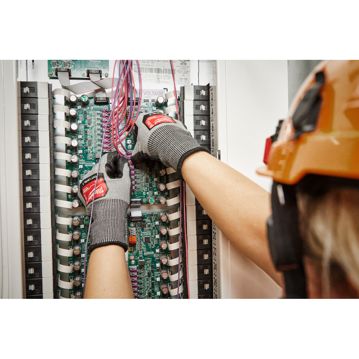 Gray and black polyurethane dipped work gloves with red Milwaukee branding worn while handling electrical panel components.