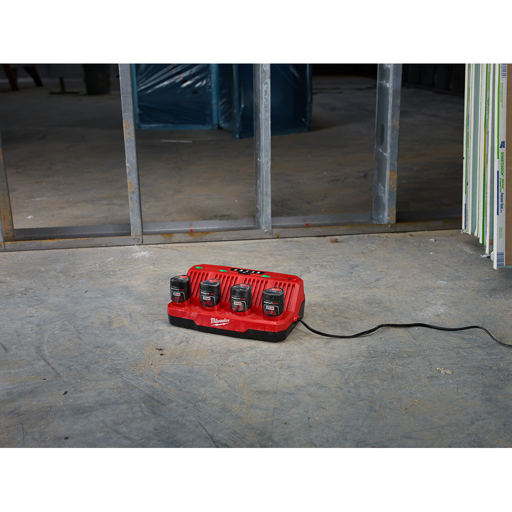 Red and black Milwaukee M12 four-bay battery charger with power cord on concrete floor.