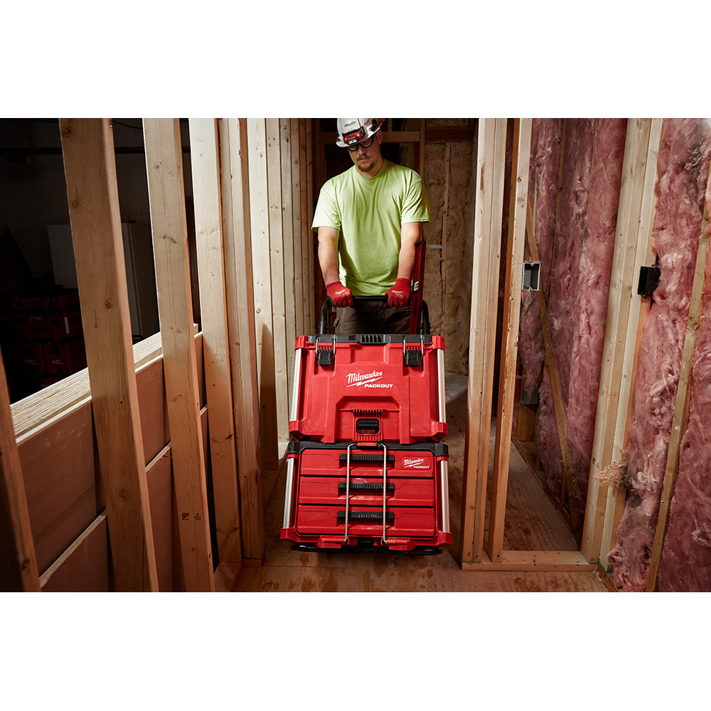 Red two-wheel cart with stacked storage boxes being pushed through a doorway by a worker in a construction site.