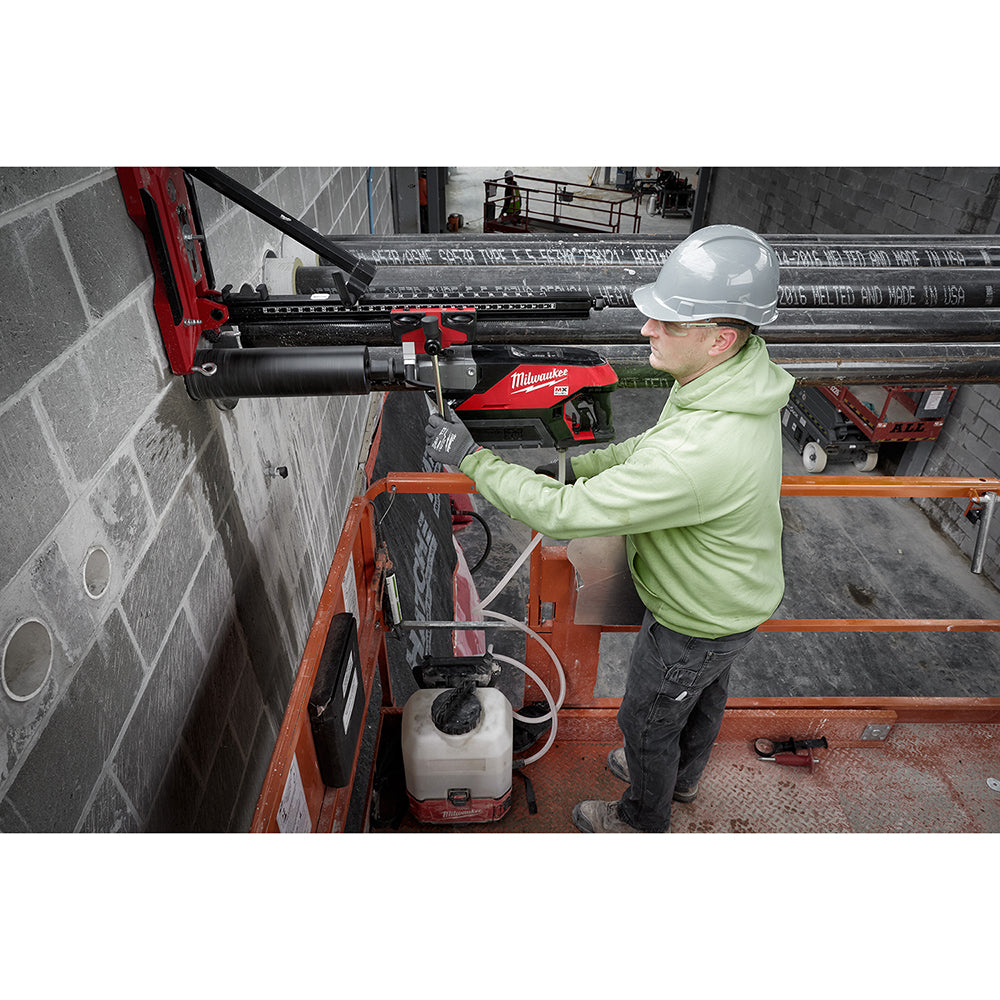 Milwaukee compact core drill stand with red and black motor unit mounted on orange frame, used for drilling into concrete wal