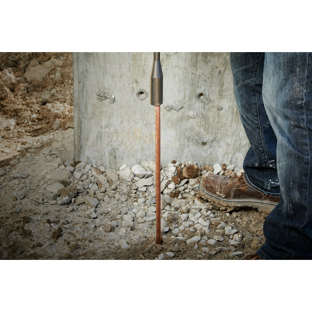 Ground rod driver with SDS+ connection inserted into rocky soil next to concrete surface.