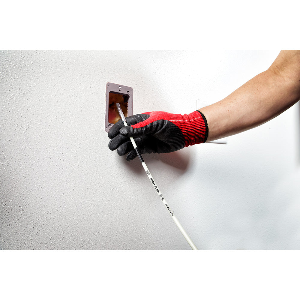 White flexible fish stick being used to route wire through a wall outlet opening, held by gloved hand.