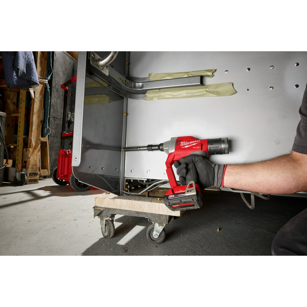 Milwaukee M18 FUEL rivet tool with red and black housing held in gloved hand in workshop setting.