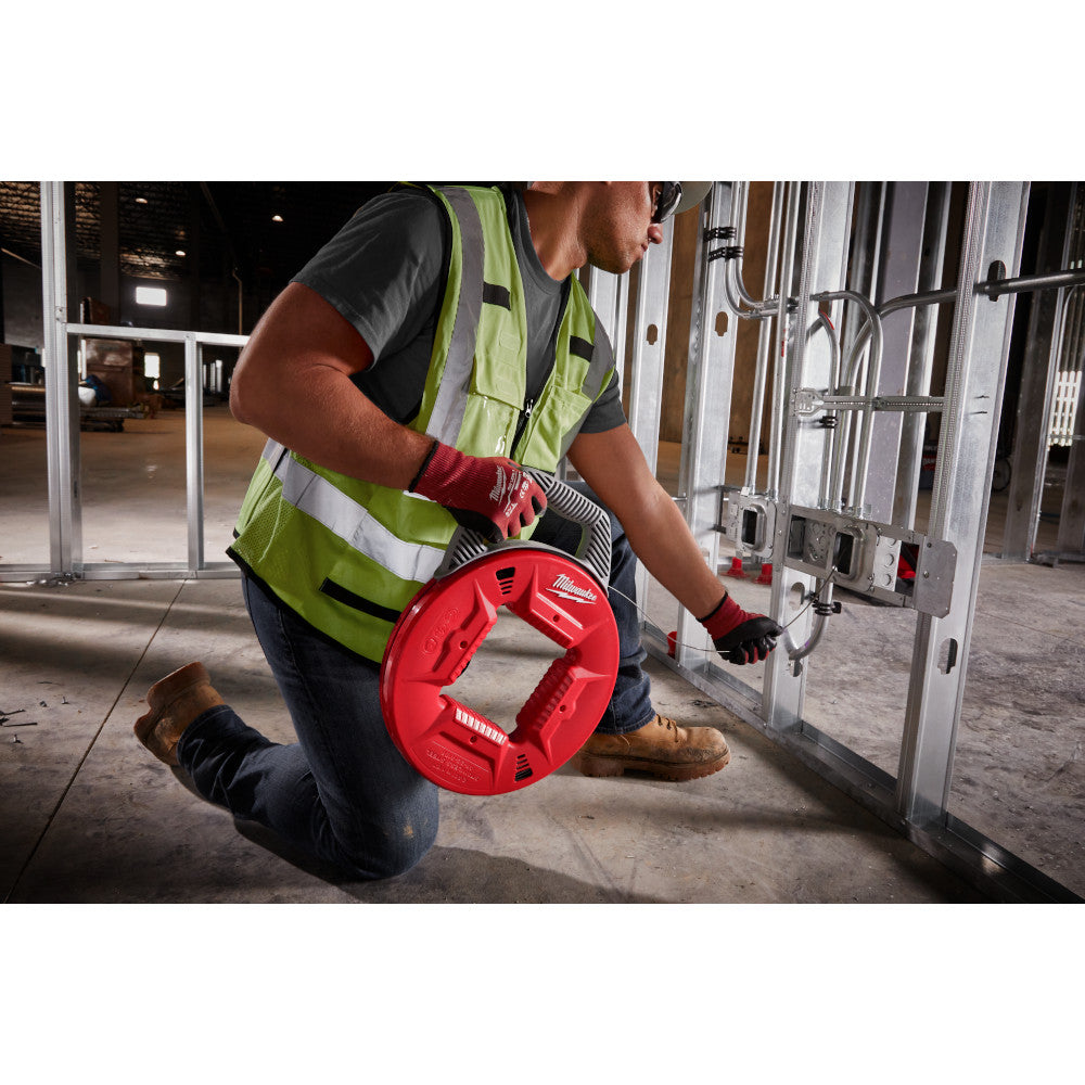 Worker in safety vest using red Milwaukee fish tape reel on metal conduit in industrial setting.
