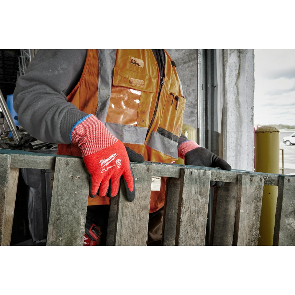 Red and black dipped work gloves with Milwaukee branding worn on wooden surface.