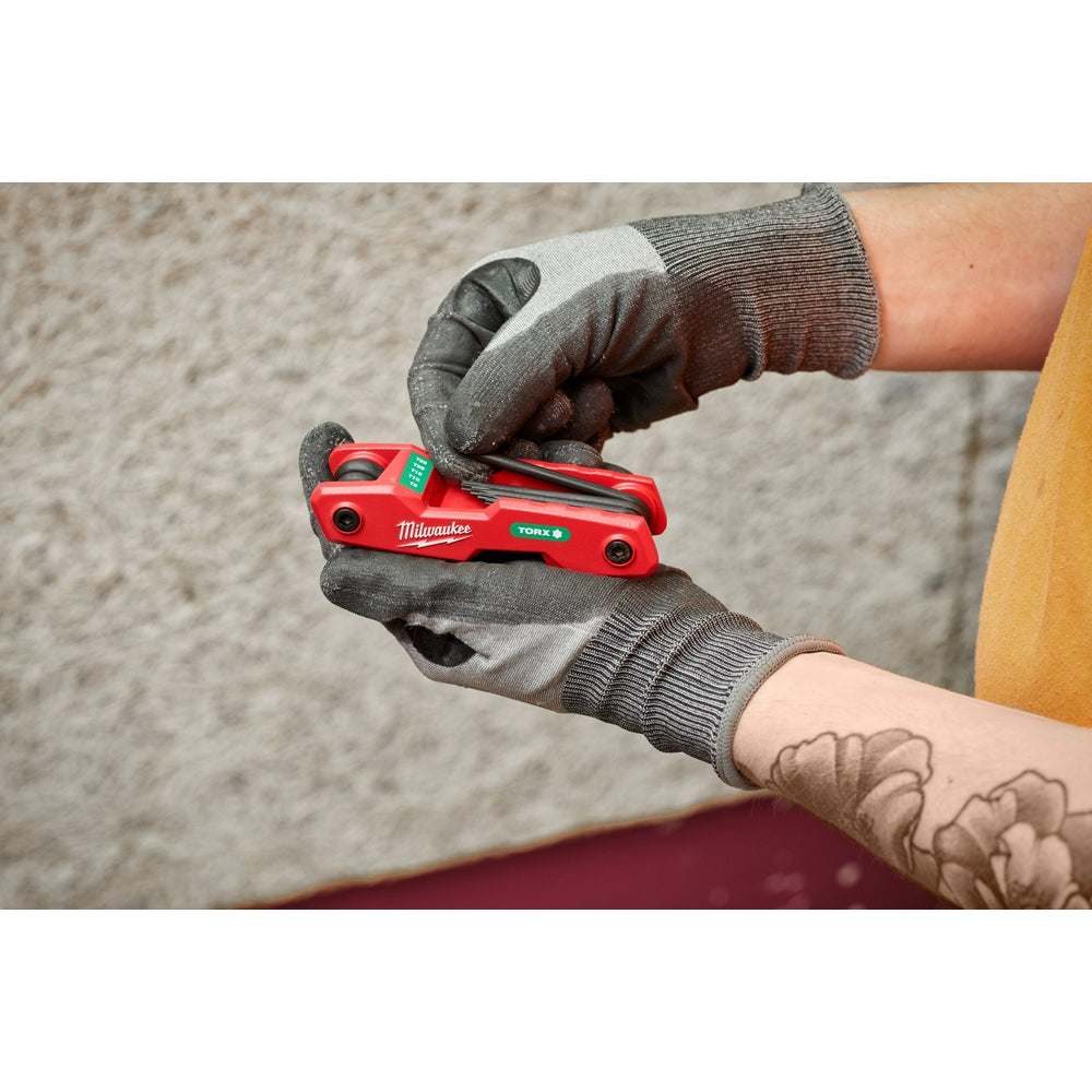 Red Milwaukee folding hex key set with eight Torx keys held in gloved hands.