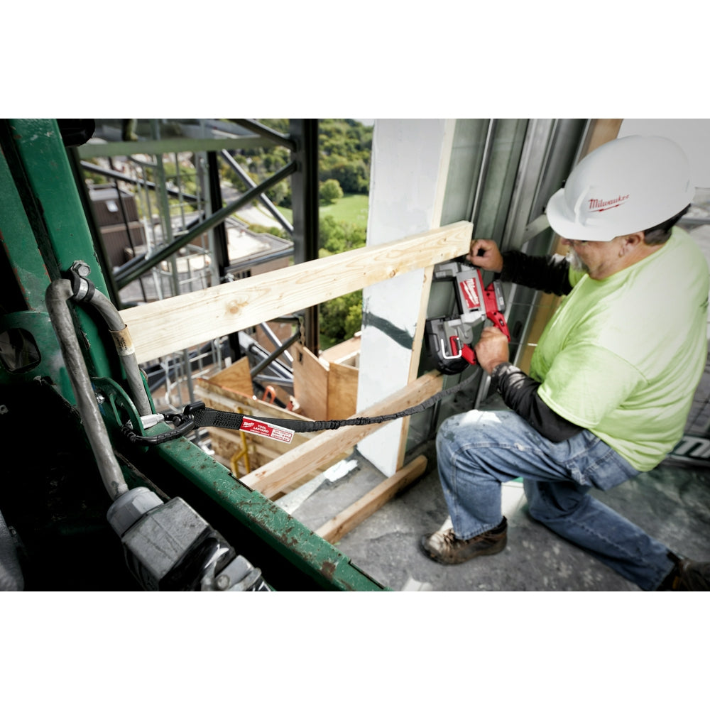Worker wearing hard hat using black locking tool lanyard attached to belt while holding power drill on elevated wooden beam.