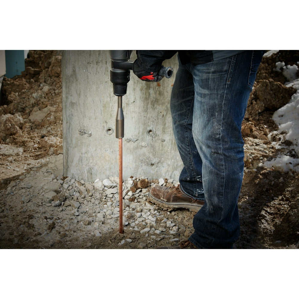 Ground rod driver bit attached to power drill being used to drive copper rod into soil.