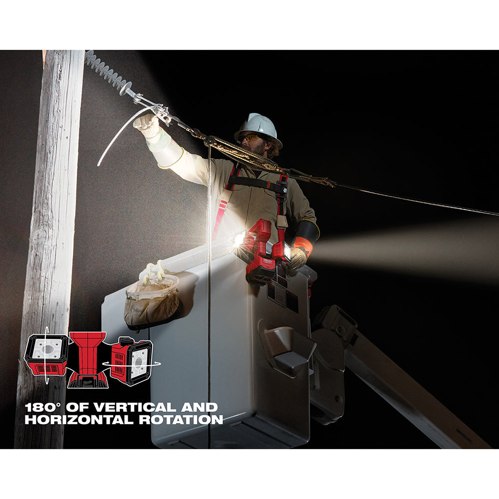 Red and black Milwaukee work light mounted on pole at night, illuminating work area with bright white beam.