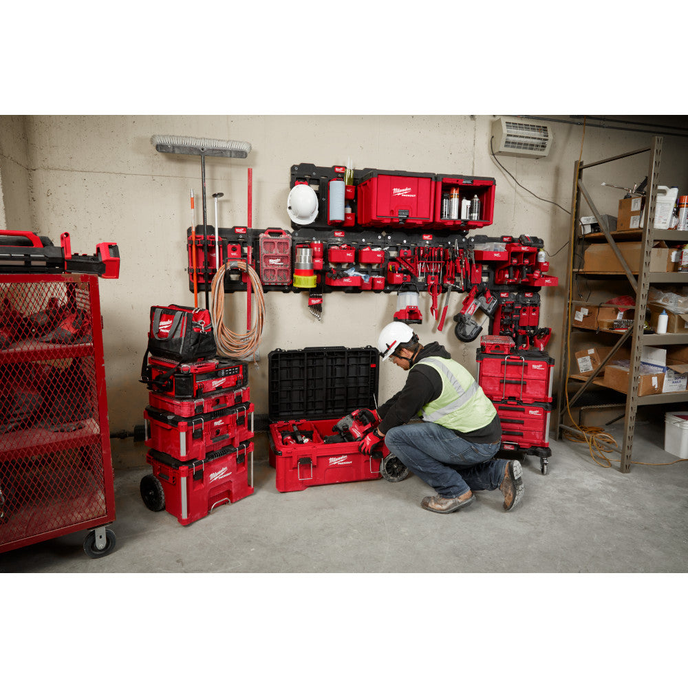 Red and black Milwaukee PACKOUT wall plate mounted on concrete wall holding tools and storage components in workshop.