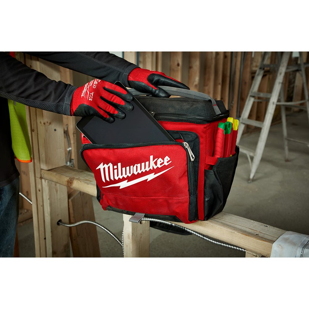 Red and black Milwaukee jobsite cooler with carrying handle and side storage pockets on wooden workbench.