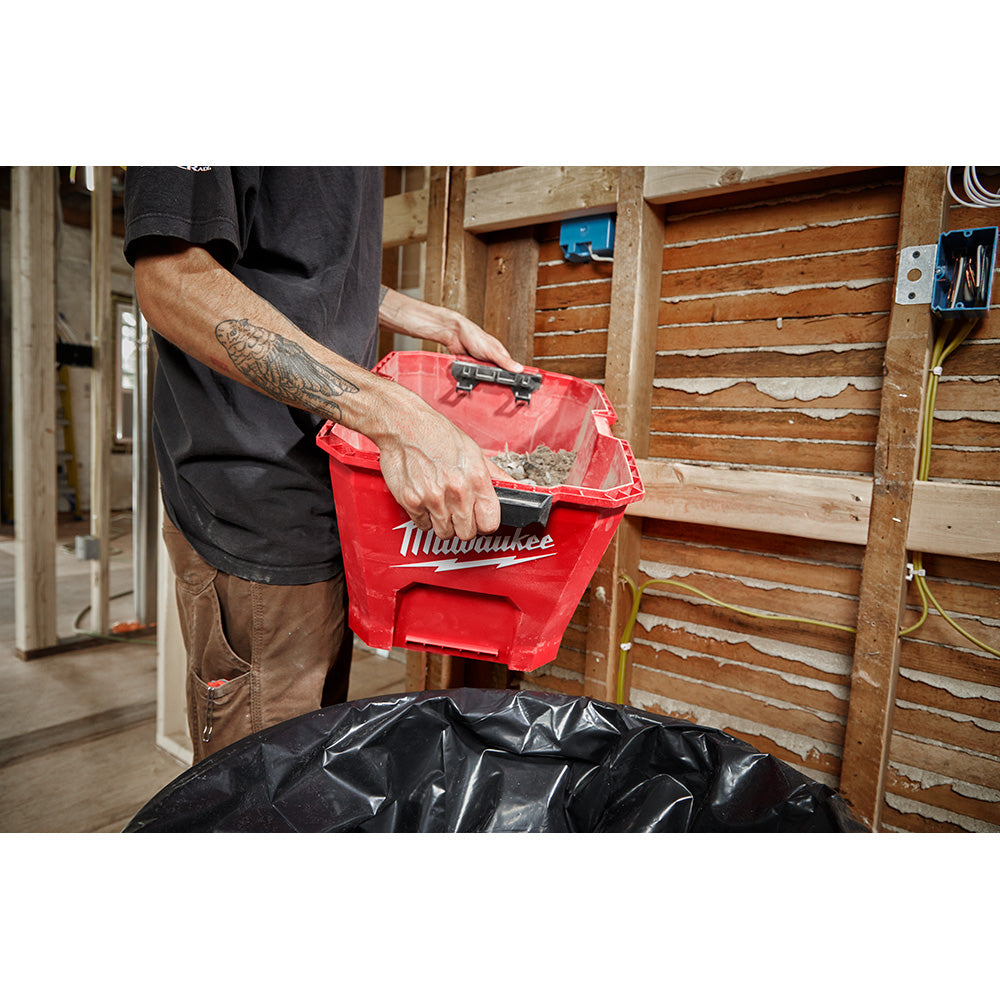 Red Milwaukee wet/dry vacuum tank with black collection bag being held by person in workshop.