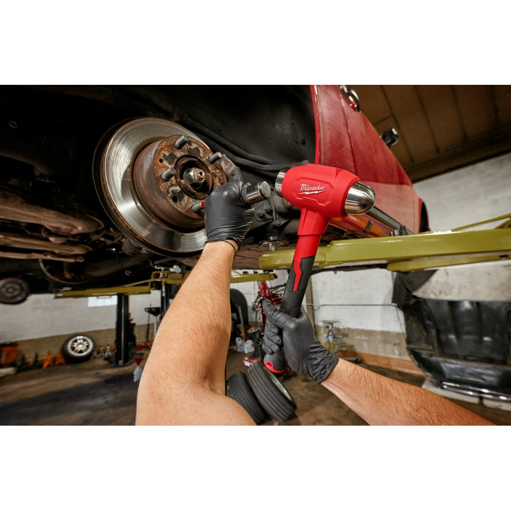 Red and black Milwaukee dead blow hammer with ball peen head held in mechanic's hand above vehicle brake rotor.