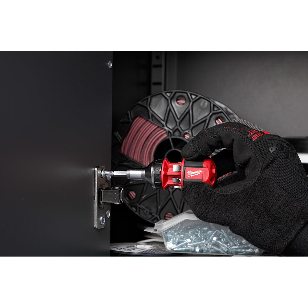 Red and black ratcheting multi-bit driver being held in gloved hand against electrical outlet.