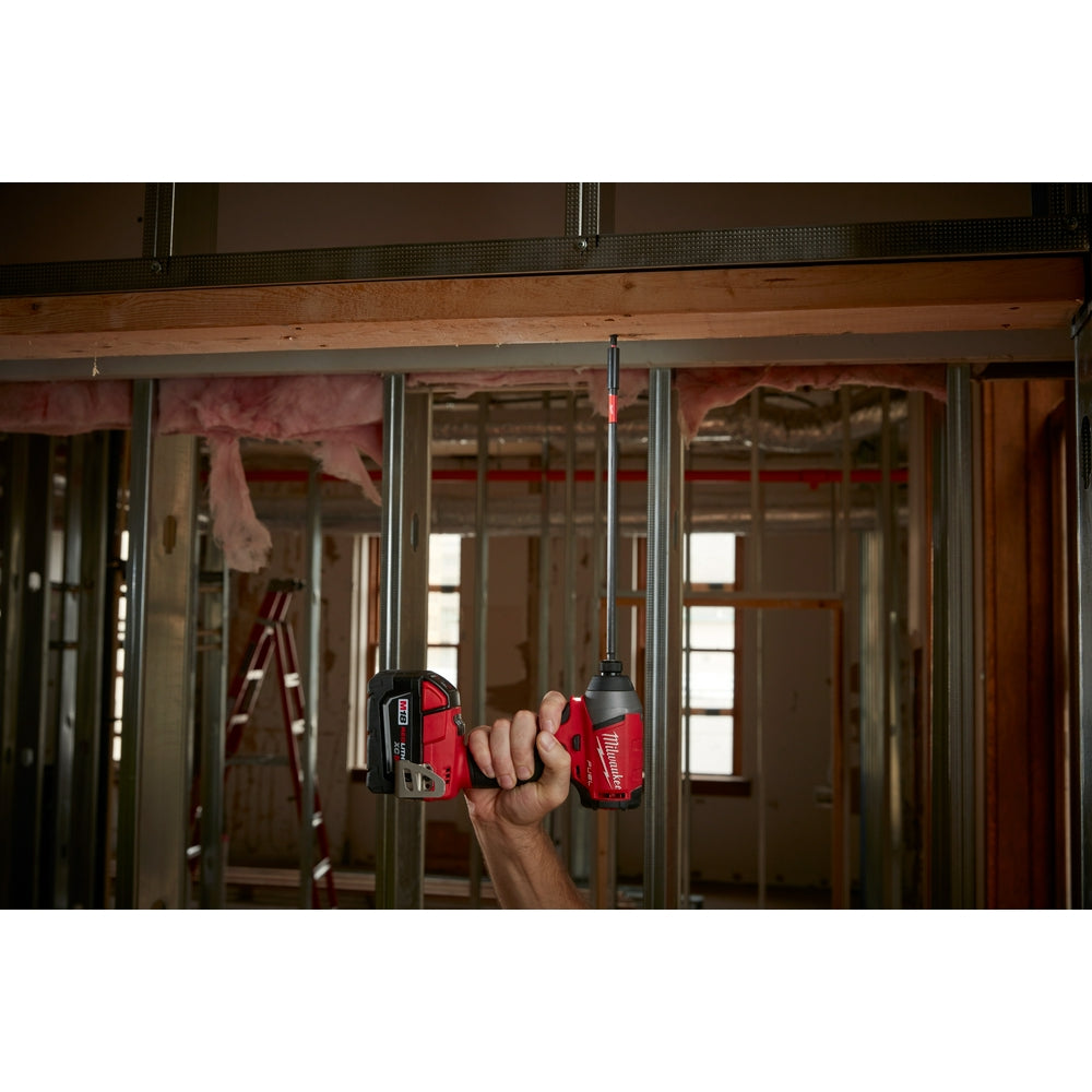 Red and black magnetic bit holder suspended from cord, held in hand against construction site background.