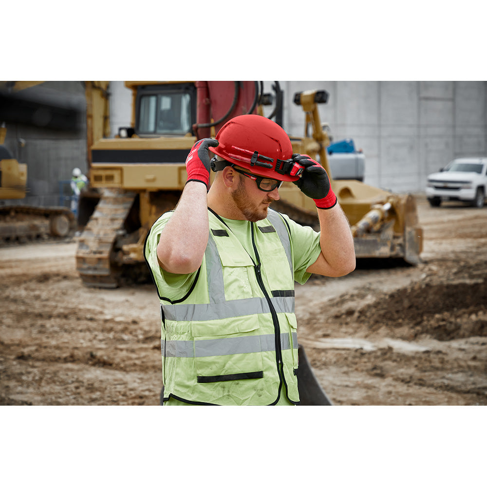 Orange full brim hard hat with black ratcheting suspension straps worn by construction worker on job site.