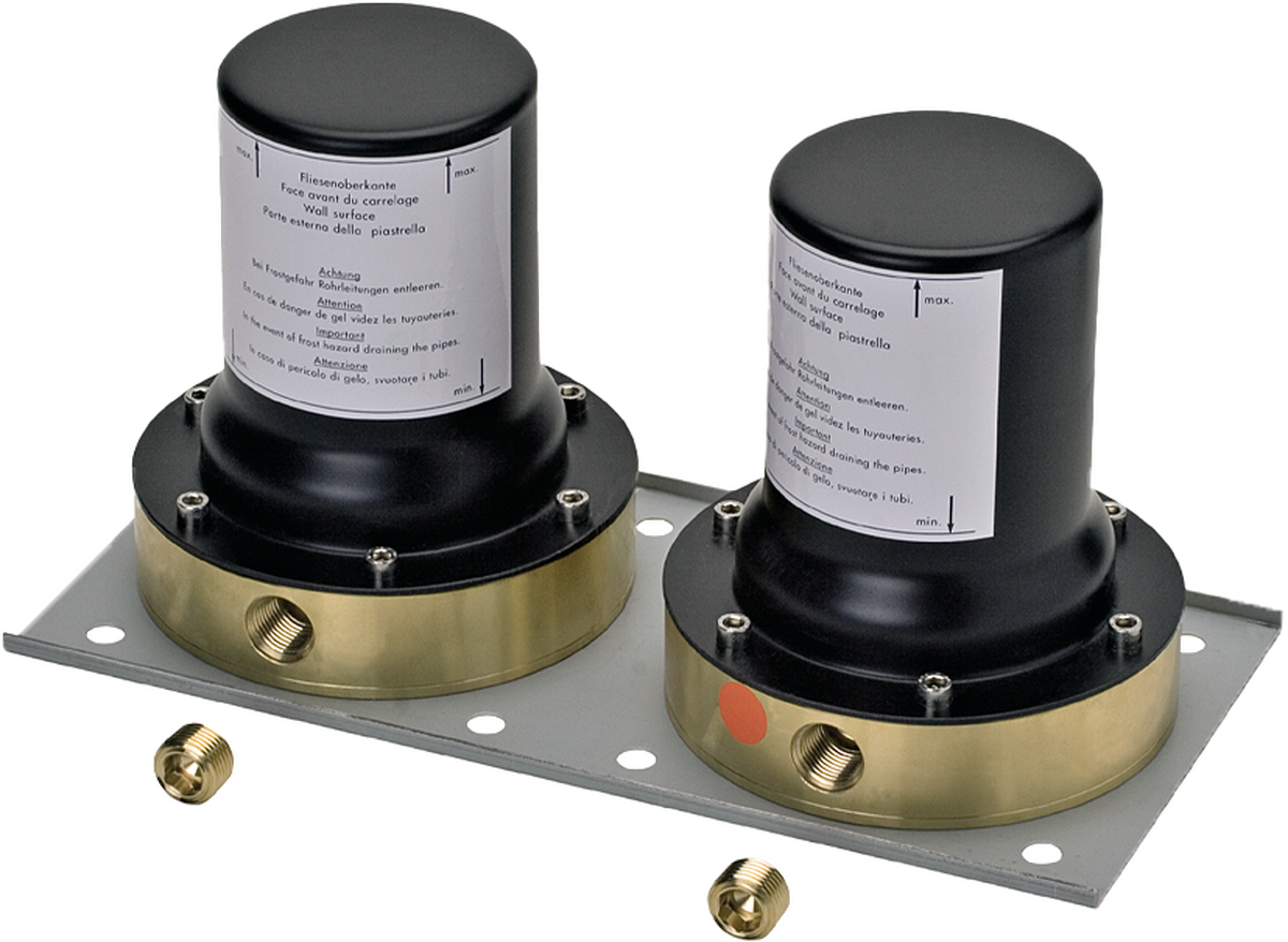 Two black and brass cylindrical valve bodies with instruction labels mounted on gray metal plate with brass fittings.