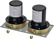 Two black and brass cylindrical valve bodies with instruction labels mounted on gray metal plate with brass fittings.