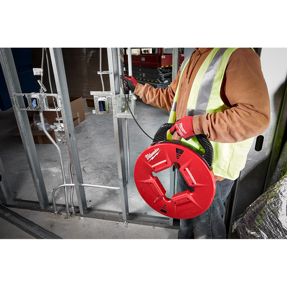 Worker holding red Milwaukee fish tape reel with polyester tape extended toward electrical conduit.