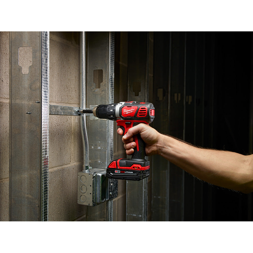 Red and black Milwaukee M18 cordless drill driver with battery, held in hand while drilling into metal stud framing.