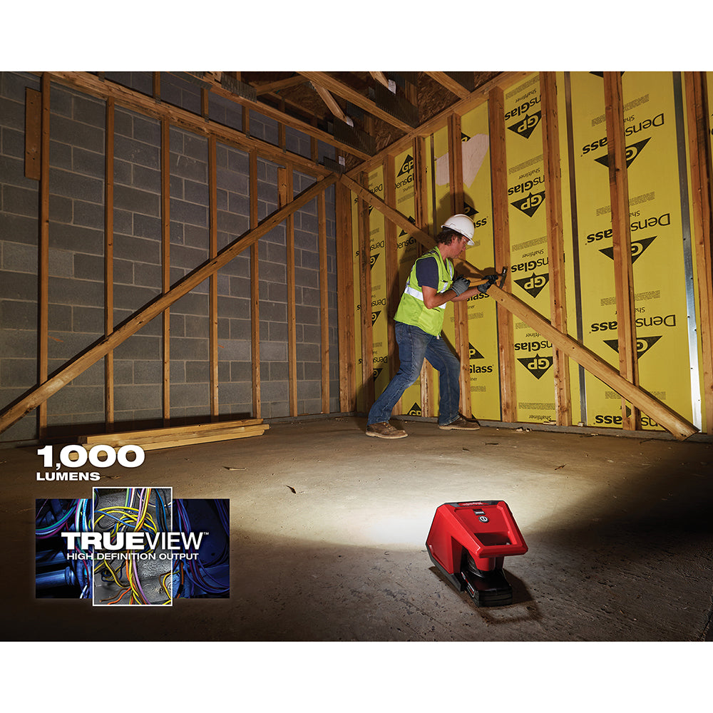 Red Milwaukee M12 compact flood light illuminating an interior construction area with worker in background.