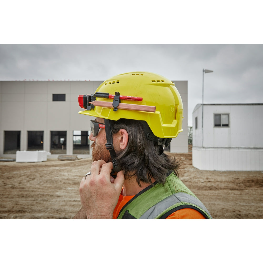 Gray vented hard hat with front brim and red BOLT attachment, worn on construction site.