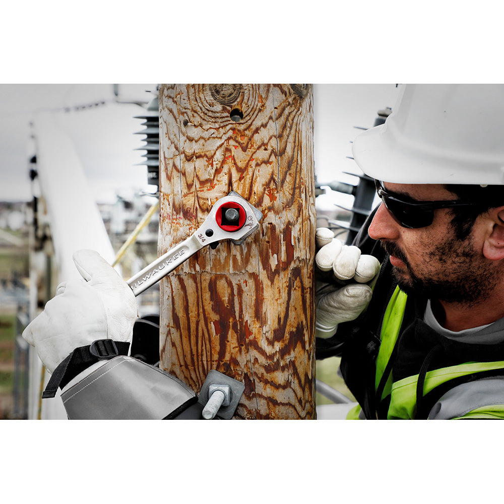 Milwaukee ratcheting wrench with red head and milled strike face held against wooden pole by worker in safety gear.
