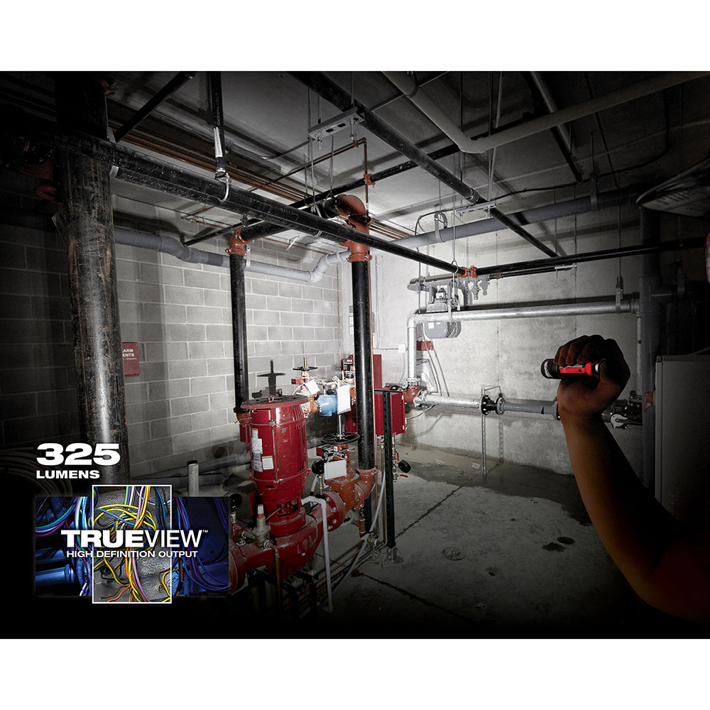 Black and red LED flashlight held in hand, illuminating an industrial warehouse space with equipment.