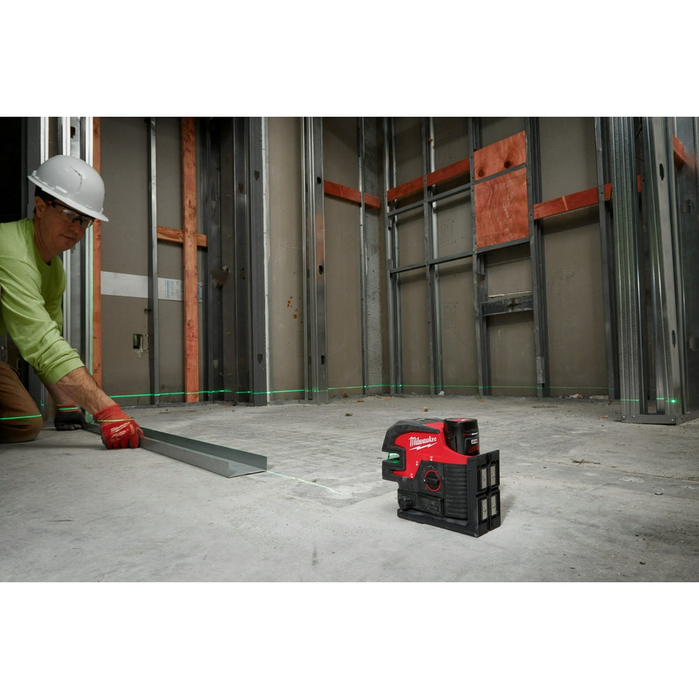 Red and black Milwaukee laser level projecting green cross lines on concrete floor during construction work.