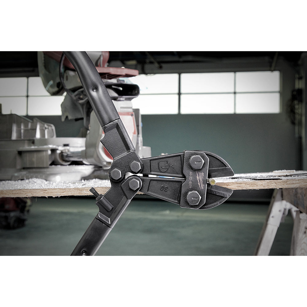 Black bolt cutter with long handles positioned on wooden work surface in workshop setting.