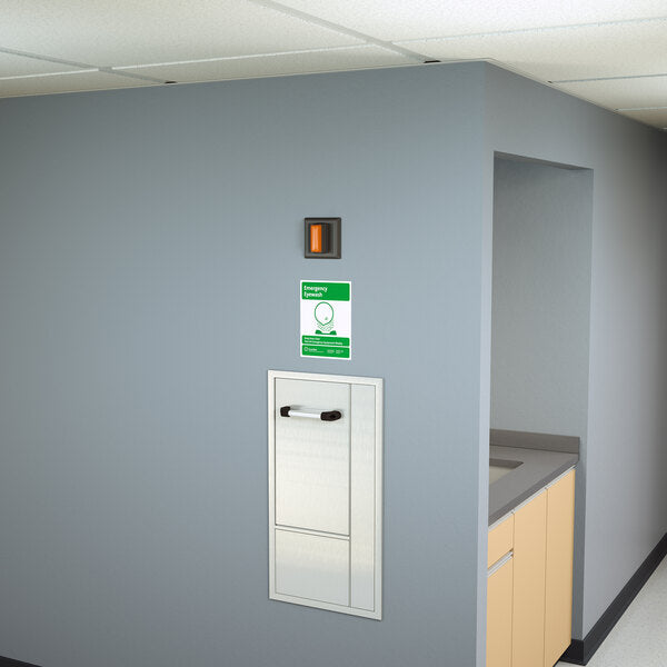 Stainless steel recess-mounted swing-down eye wash station with drain pan mounted on interior wall above wooden counter.
