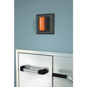 Dark gray alarm unit with illuminated orange indicator light mounted on blue wall above safety shower station.
