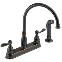 Oil-rubbed bronze kitchen faucet with curved spout, two handles, and side spray attachment.