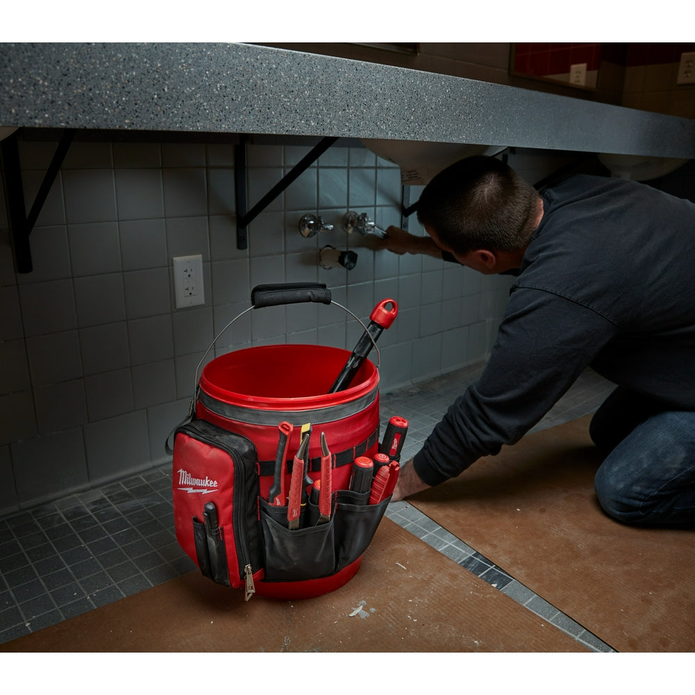 Red and black bucket organizer bag with multiple storage pockets attached to a red bucket, displayed in a bathroom setting.