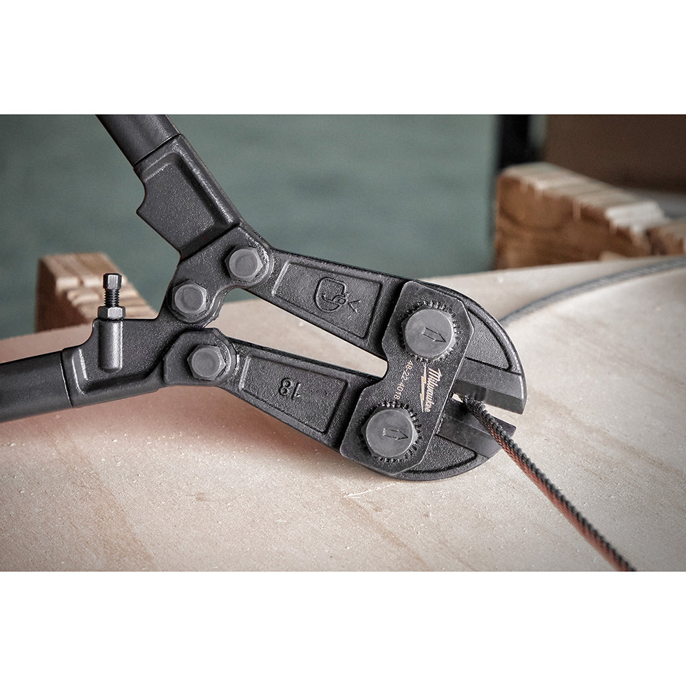 Black metal bolt cutter with handles positioned over a rope on a wooden surface.