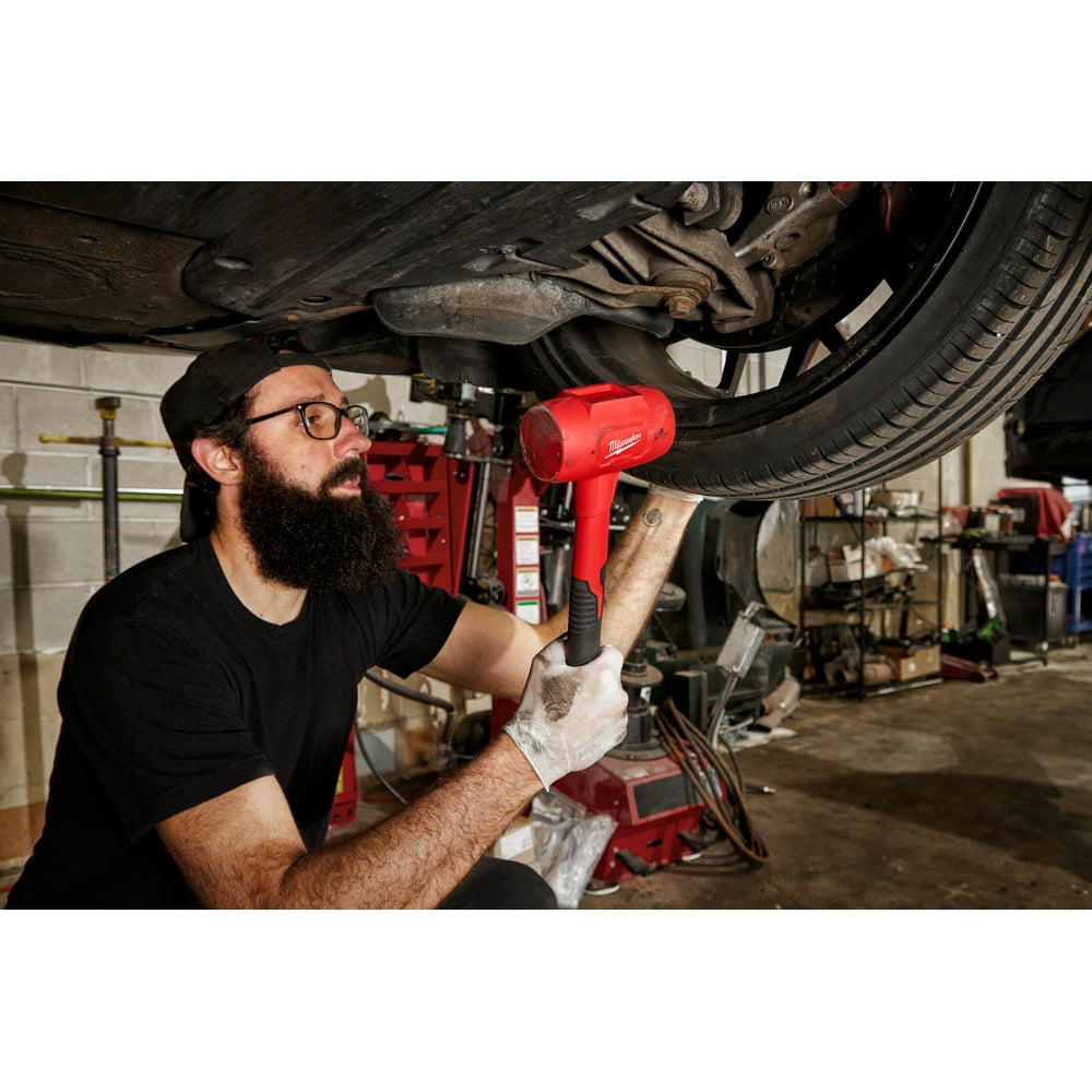 Red dead blow hammer with black grip being used on vehicle undercarriage in workshop.