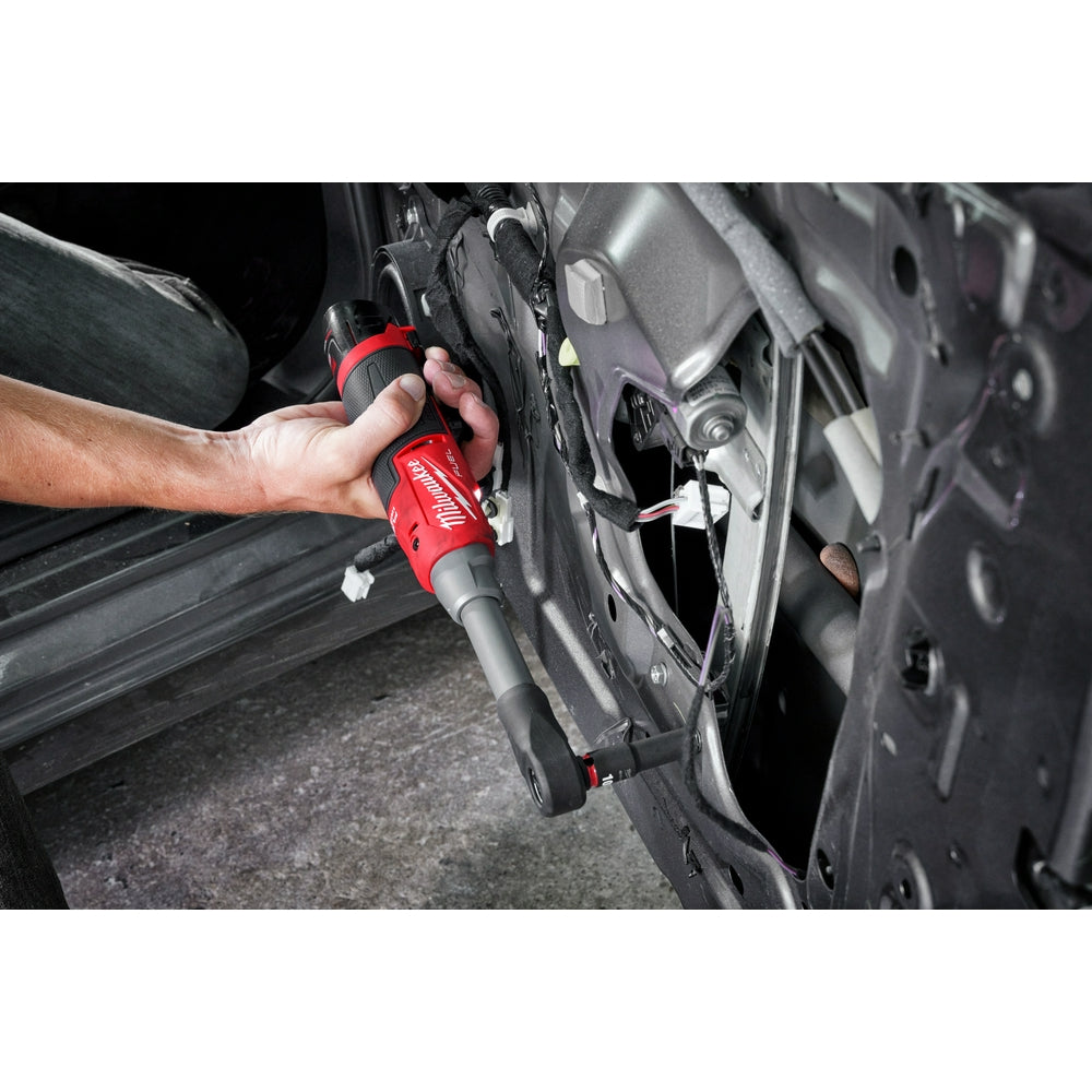 Hand holding red and black Milwaukee cordless ratchet with protective boot near vehicle wheel.