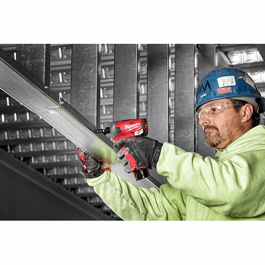 Worker in safety gear holding Milwaukee power drill and wrench on metal beam.