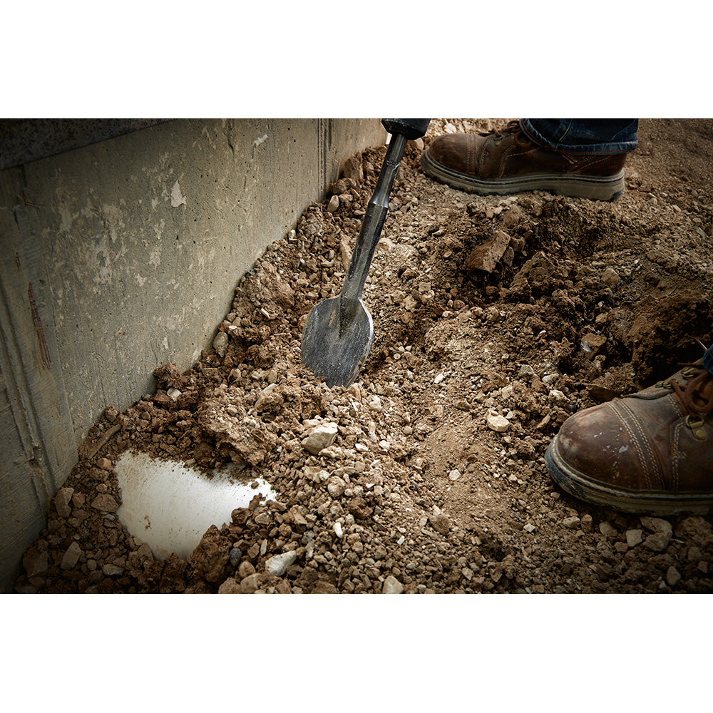SDS-Max clay spade with flat blade inserted into clay soil next to concrete foundation.