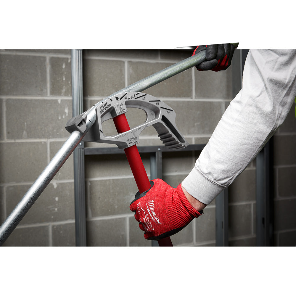 Milwaukee 1" EMT aluminum conduit bender with red handle held in gloved hands against brick wall.