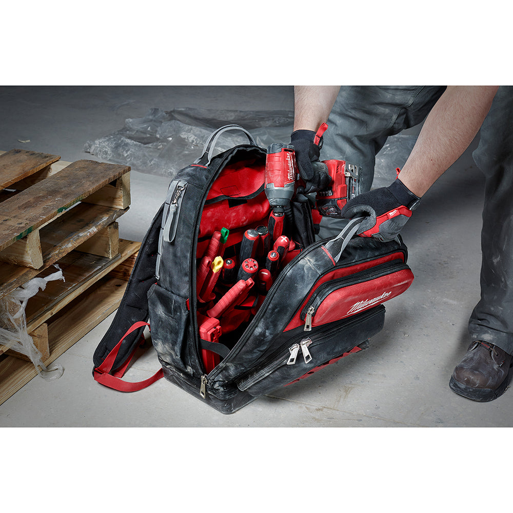 Black and red backpack with open compartments displaying tools including drills, screwdrivers, and other equipment inside.