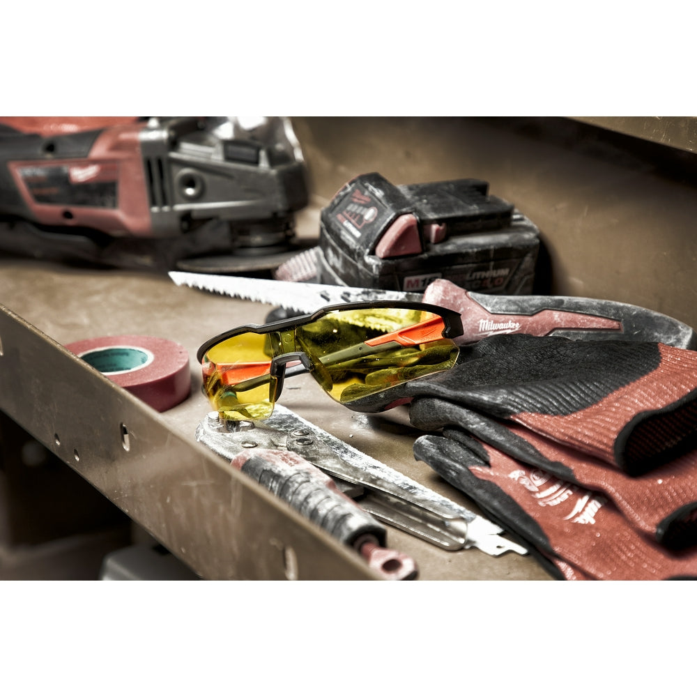 Safety glasses with yellow lenses and black frames resting on a work surface with tools.