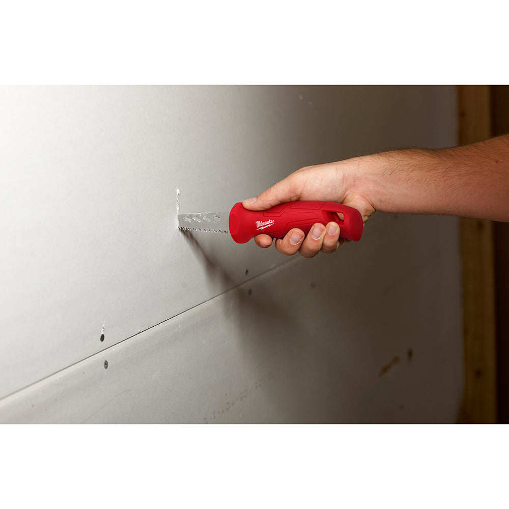 Red Milwaukee rasping jab saw with serrated blade held in hand against drywall.
