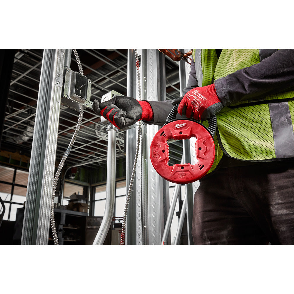 Worker in safety vest and gloves holding red fish tape reel with metal conduit in background.